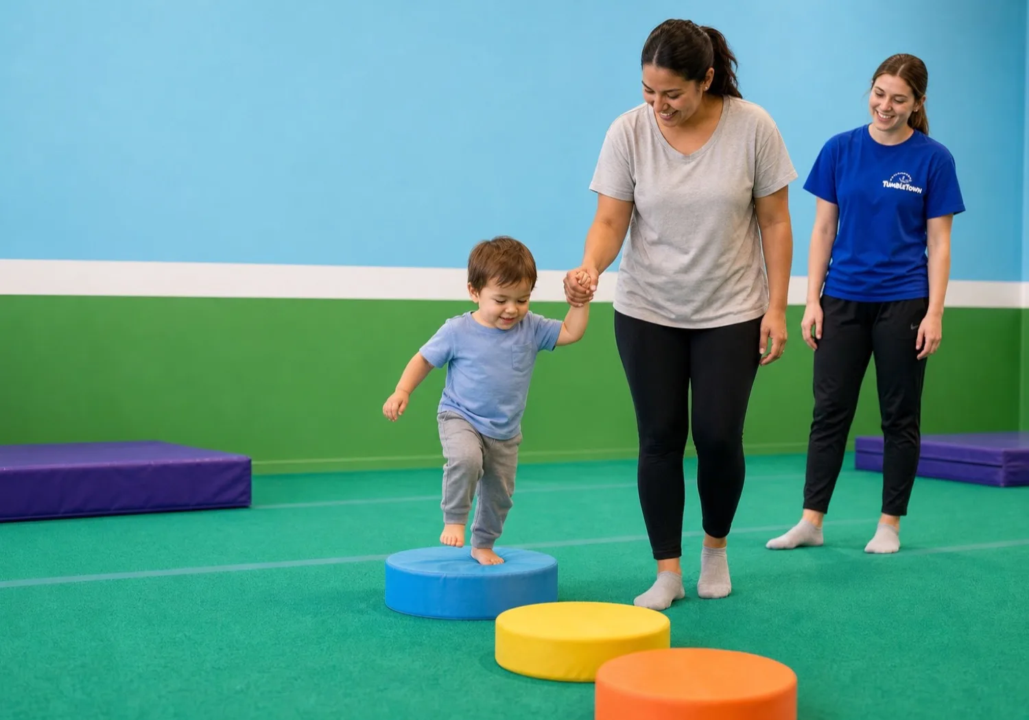 Toddler stepping onto a foam shape with a caregiver as a TumbleTown coach watches