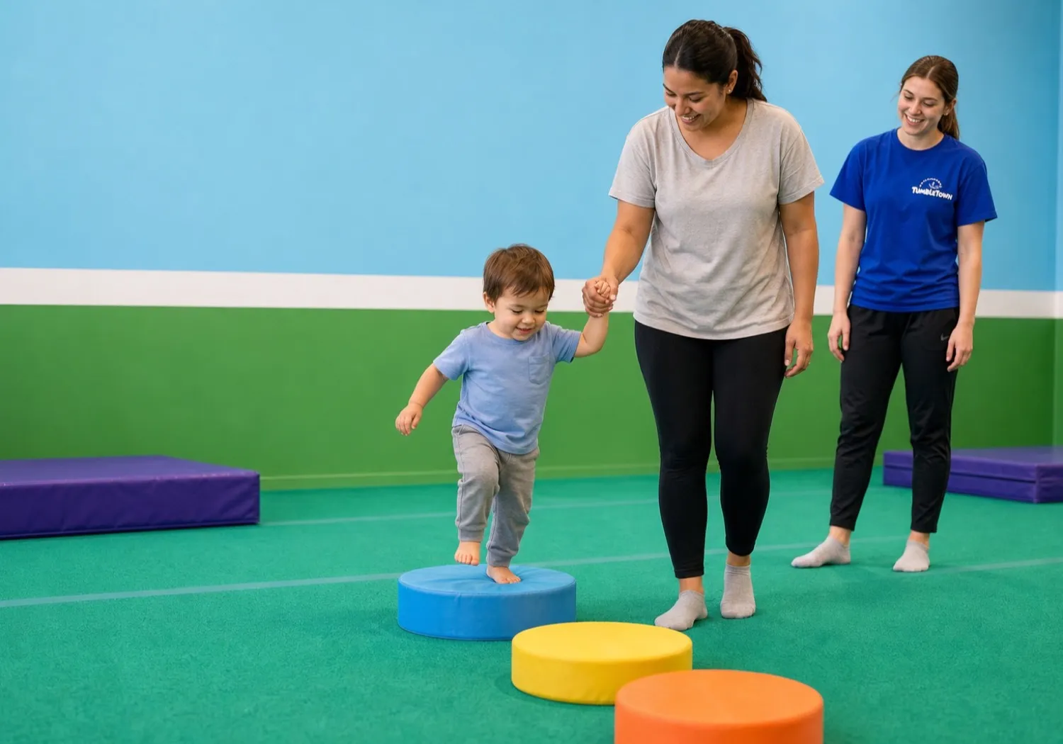 Toddler stepping onto a foam shape with a caregiver as a TumbleTown coach watches
