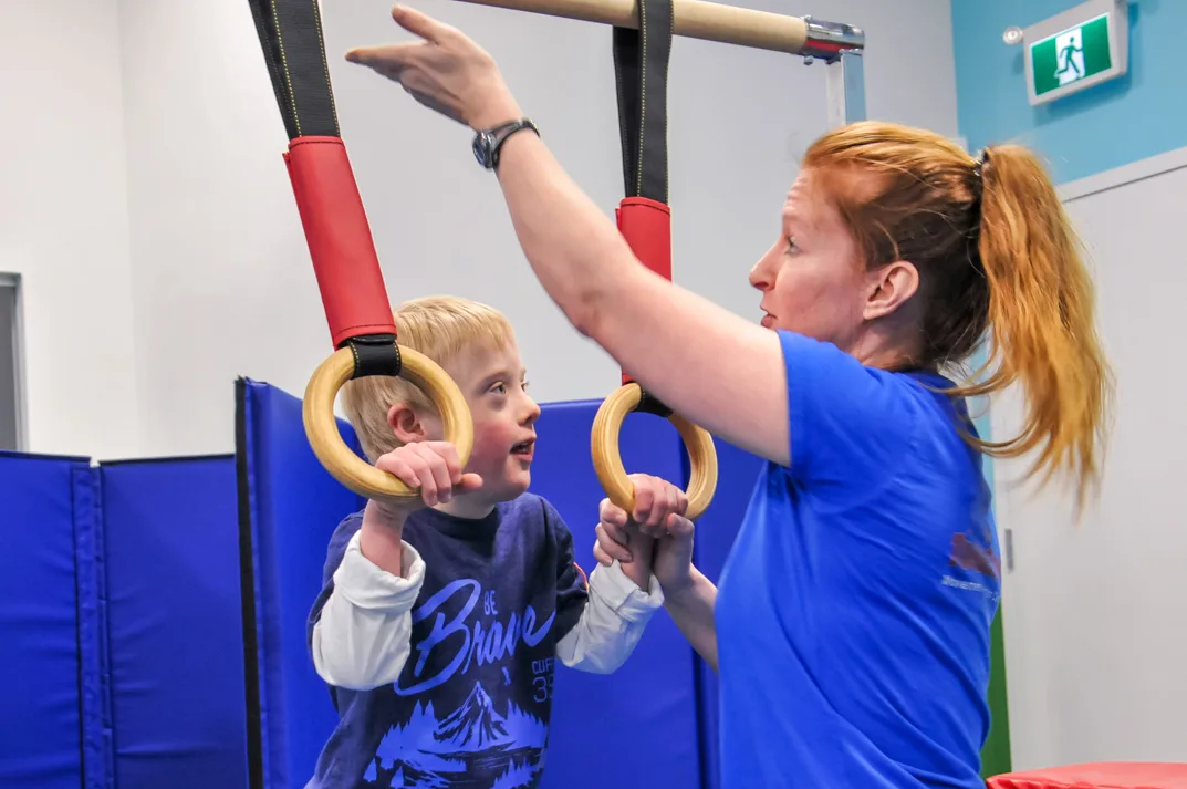 Coach guiding a boy on the rings in the Infinity Program
