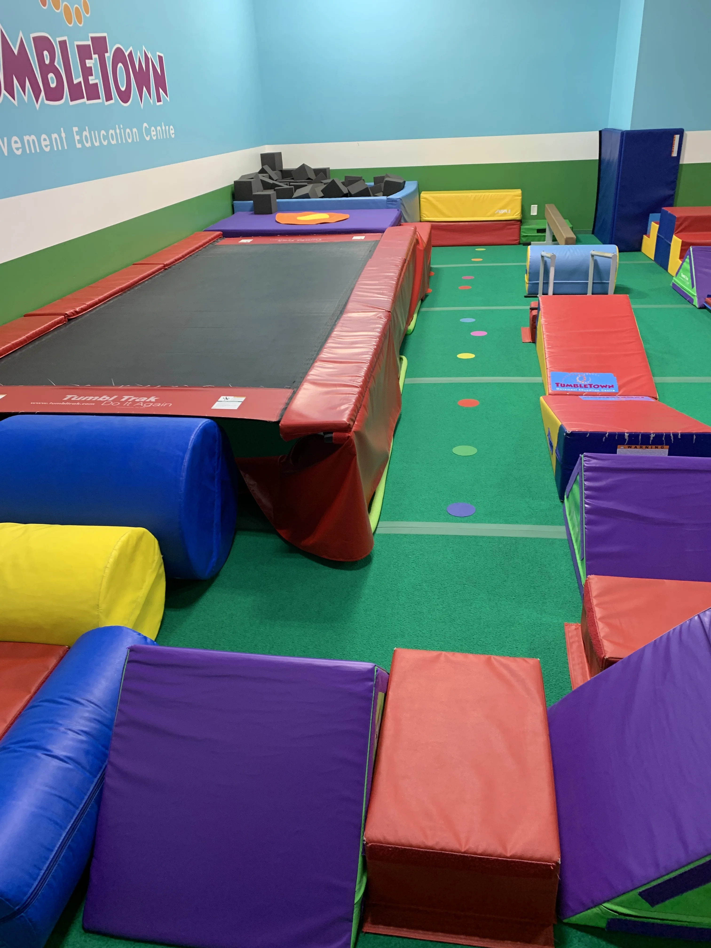 The real Kitsilano gym floor — in-ground trampoline, foam pit and colourful circuit blocks under the TumbleTown wall