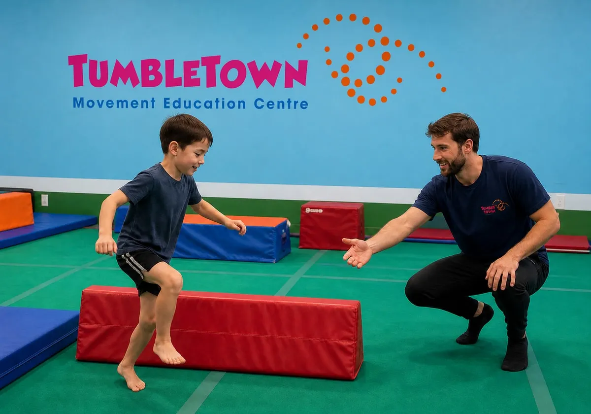 Eight-year-old stepping over a low padded obstacle with a male TumbleTown instructor nearby