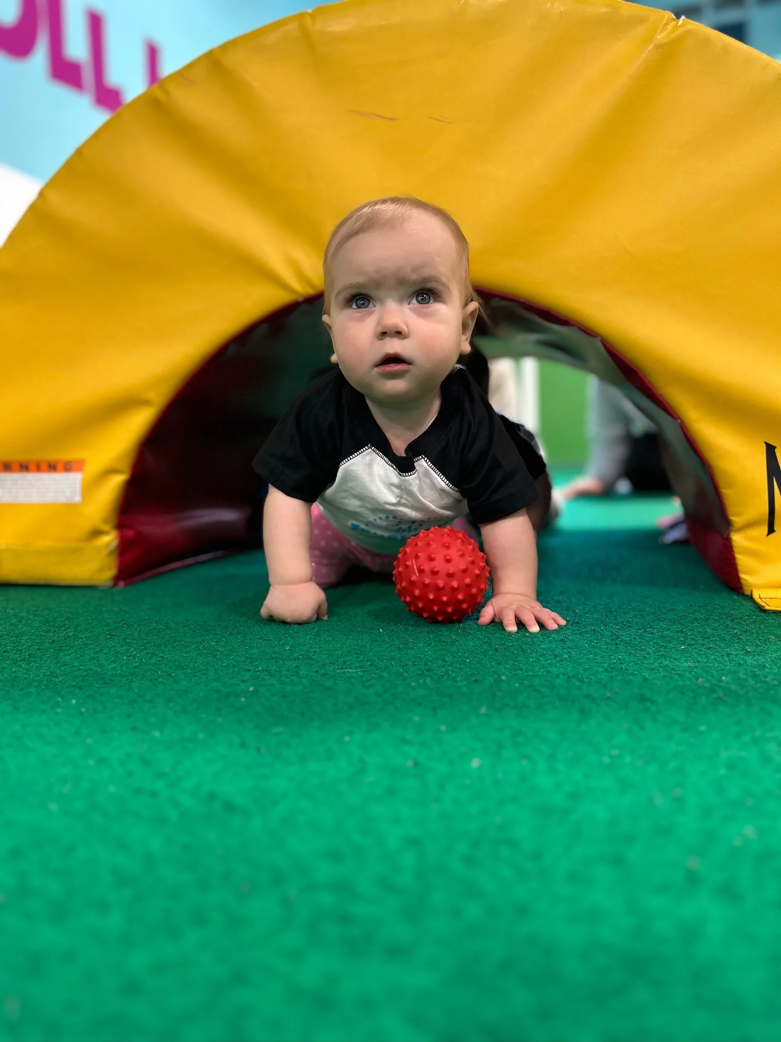 A baby crawling through a soft tunnel during a TumbleTown class