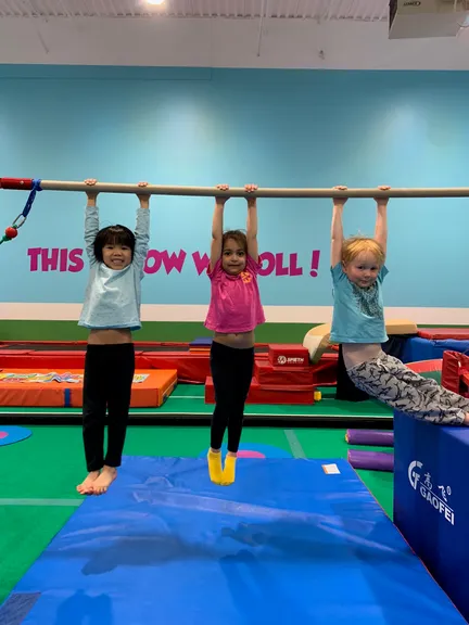 Three kids hanging from the bar, all grinning, under the THIS IS HOW WE ROLL wall