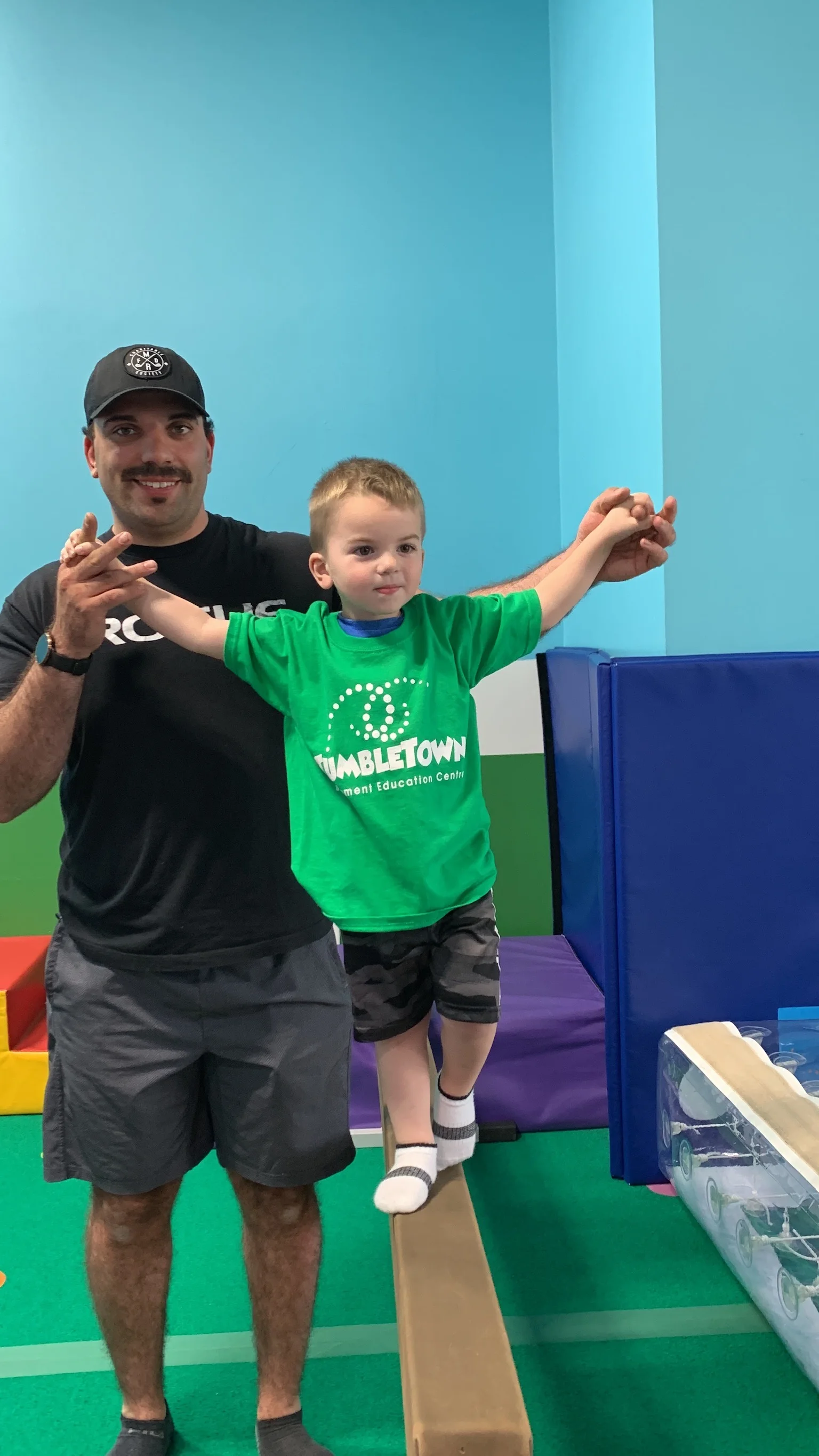 TumbleTown coach smiling with a young gymnast on a balance beam