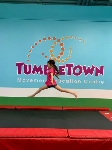 Girl mid-leap in front of the TumbleTown logo wall