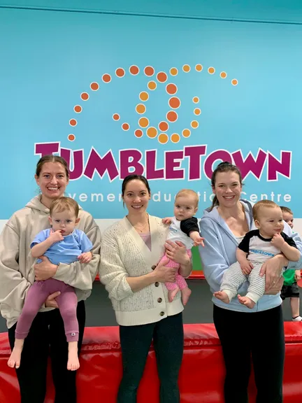 Three moms holding their babies in front of the TumbleTown logo