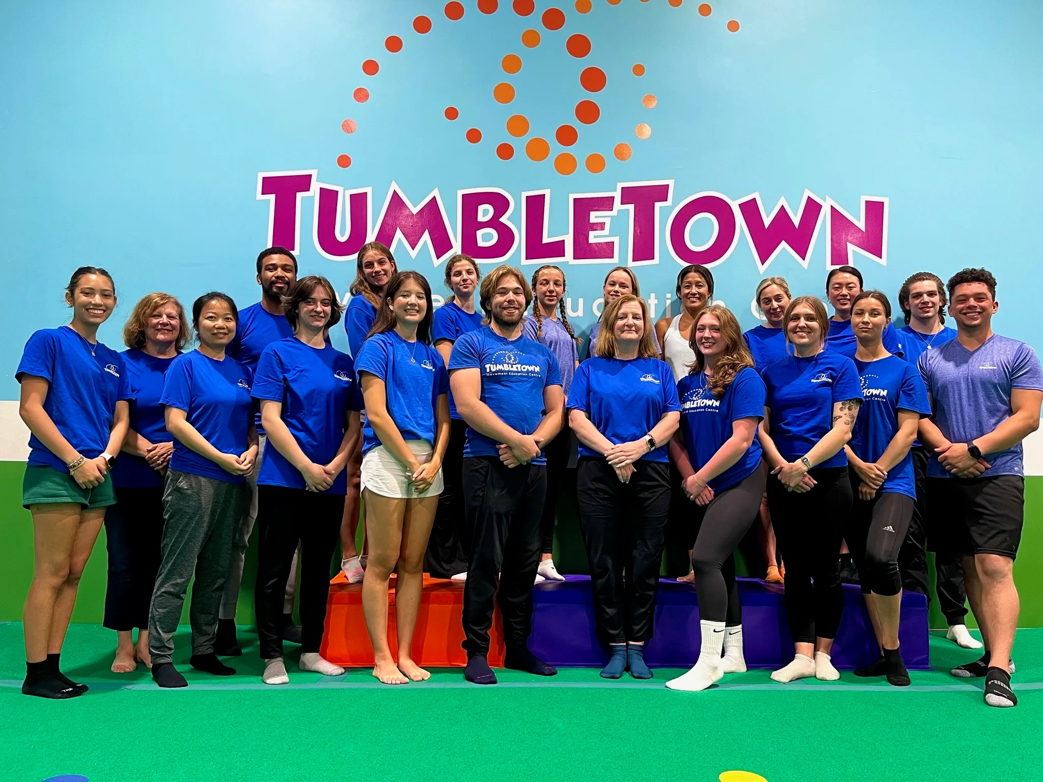 The full TumbleTown coaching team gathered under the logo wall