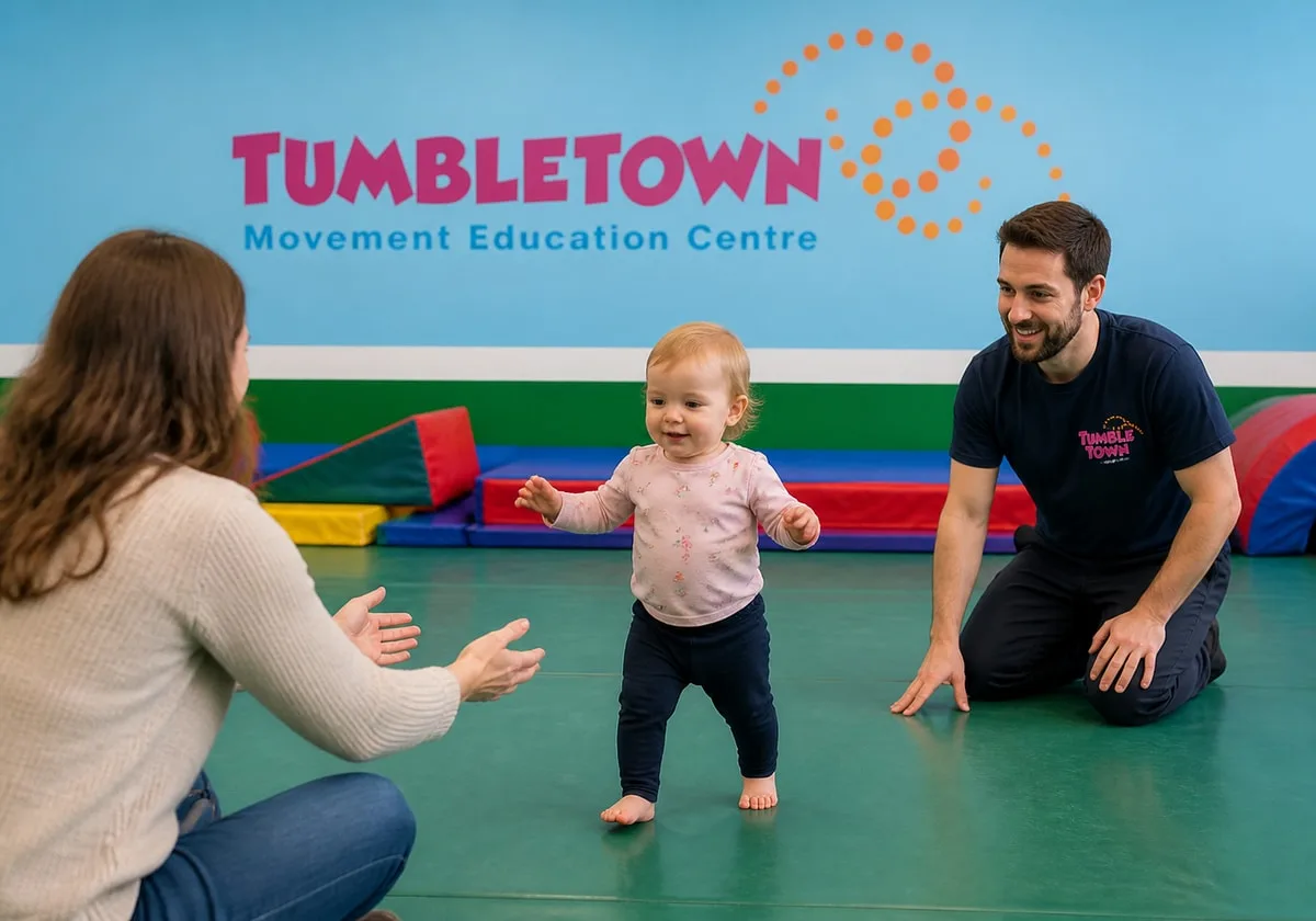Eighteen-month-old toddler walking toward a parent with a male TumbleTown instructor nearby