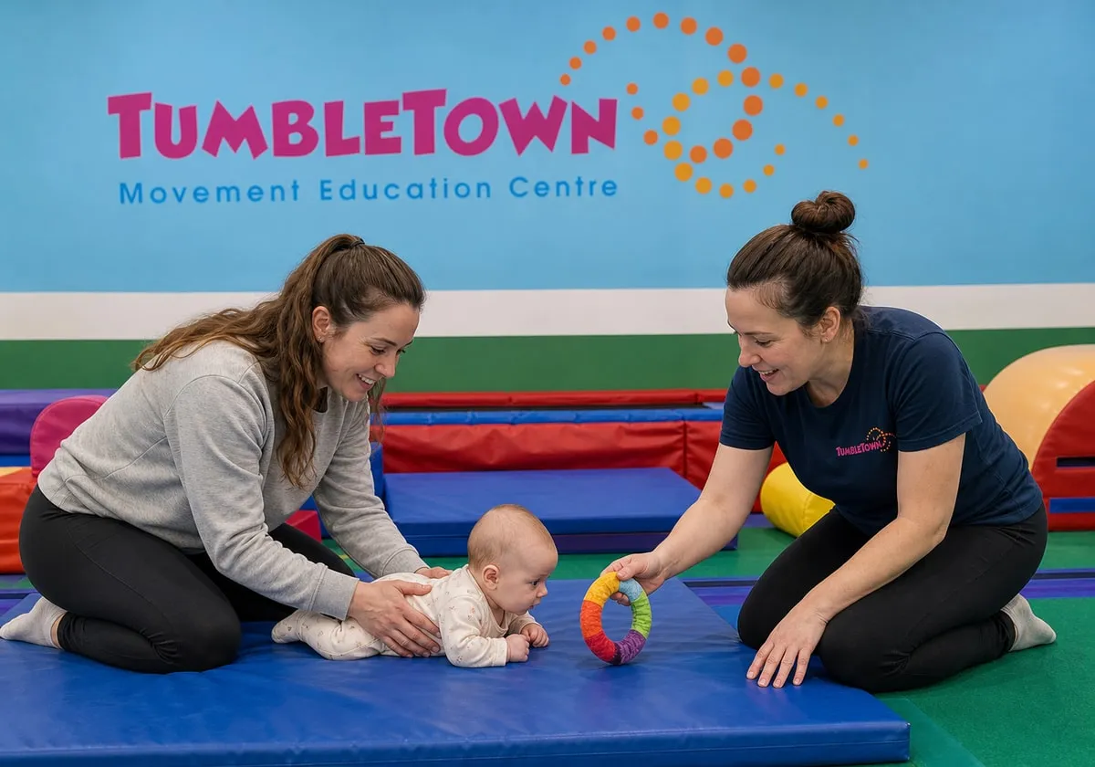 Four-month-old baby doing tummy time with a parent and female TumbleTown instructor